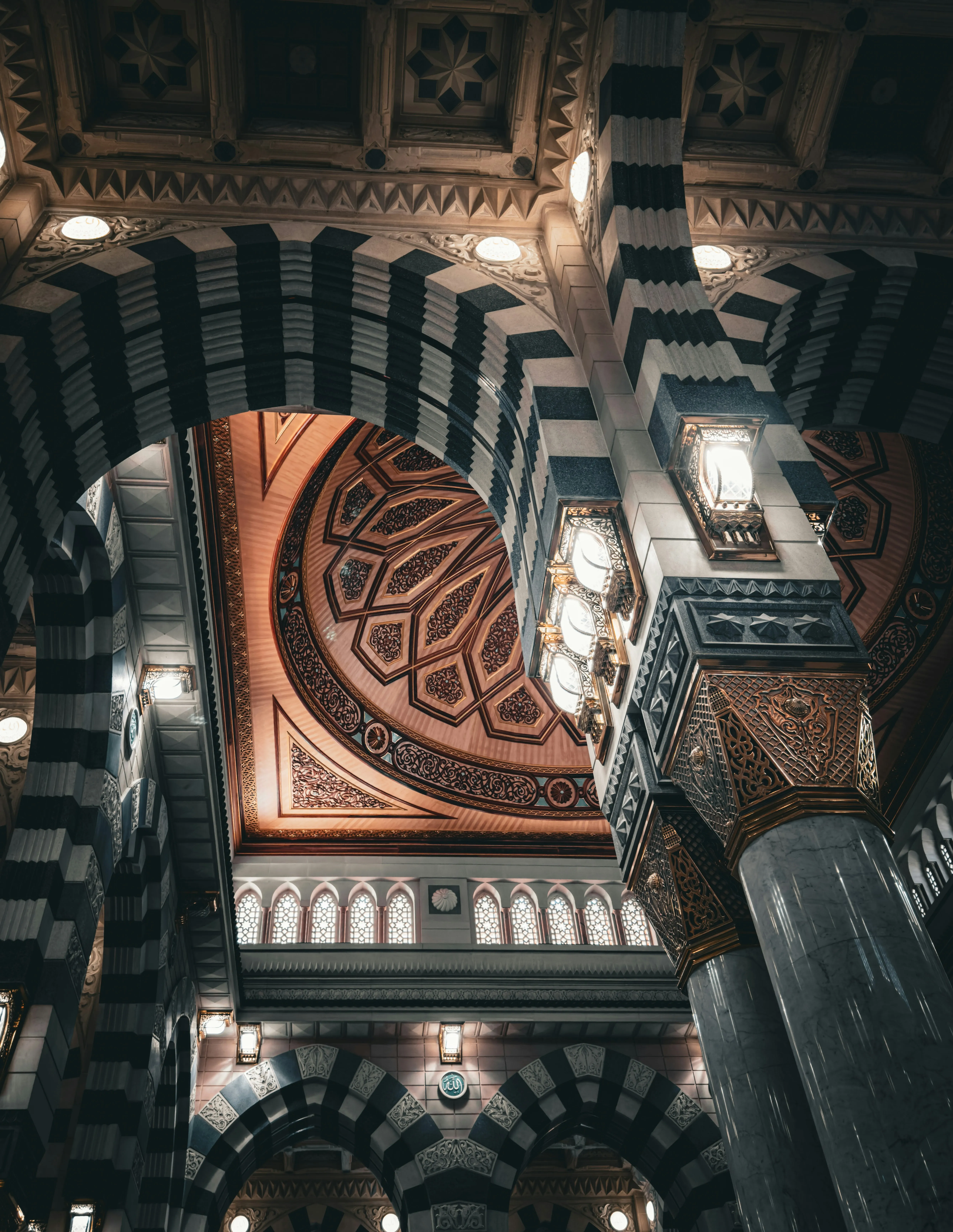 Gestreepte bogen en marmeren zuilen van al-Masjid an-Nabawi in Madinah, met een rijk versierde koepel en brandende lantaarns
