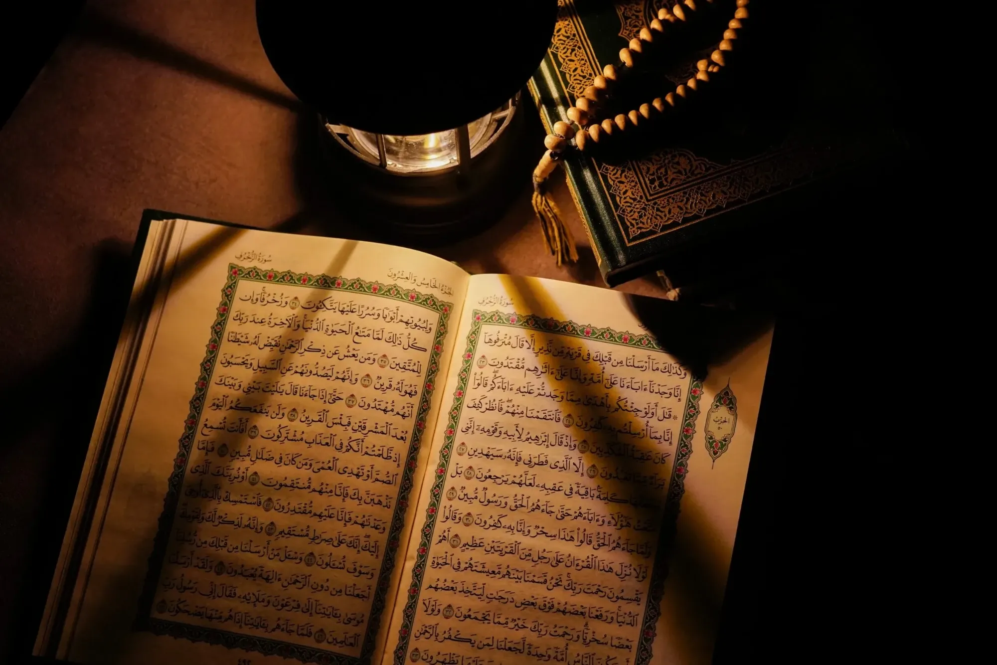 Opengeslagen mushaf in het licht van een lantaarn, met een tasbih op een gesloten boek ernaast